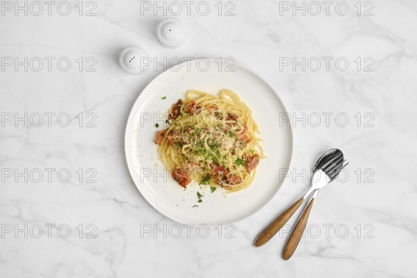 Overhead view of spaghetti carbonara sprinkled with cheese on a marble table. Salt shakers are