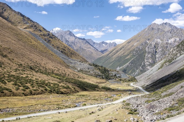 Gravel track in a valley, picturesque mountain landscape with white mountain peaks, Tian Shan