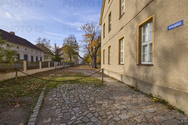 Houses with autumnal trees, square cordoned off with a rusty chain, school square, Mühlberg Elbe,