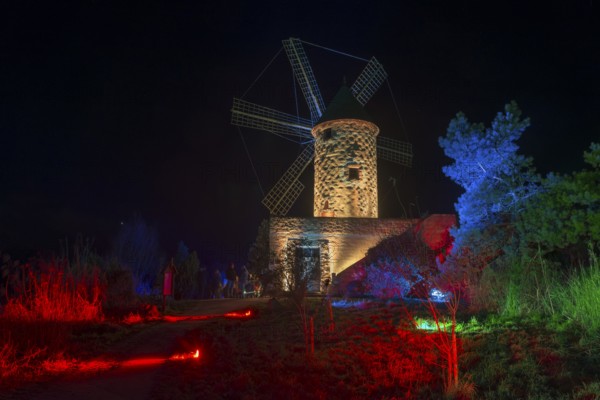Stone windmill at night in a landscape illuminated with red and blue lights, world of lights,