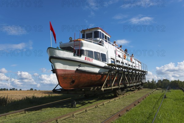 A boat on a hoist being transported over rails, under a clear summer sky, Upland Canal,
