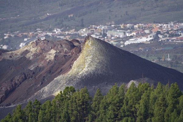 Volcanic ash cone above a cityscape, surrounded by green vegetation, last volcanic eruption of