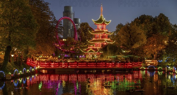 Illuminated pagoda, colourful lighting, roller coaster, trees, cityscape at night with modern