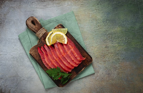 Chum salmon, cold smoked, sliced, on a cutting board, with lemon and parsley, top view, close-up,