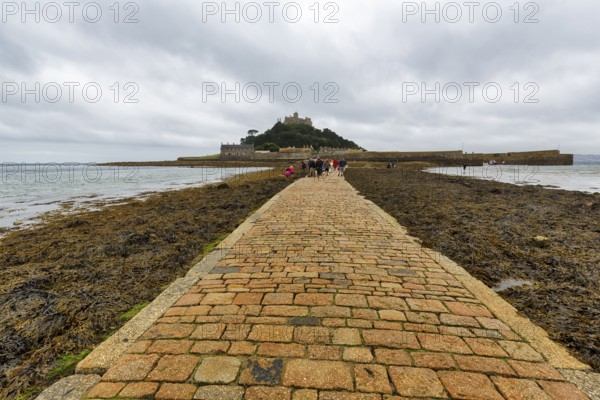 Walker, cobbled causeway, St Michael's Mount, tidal island with castle, rain clouds, Marazion,