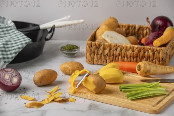 Peeled potatoes on a wooden board next to soup vegetables, preparation for cooking