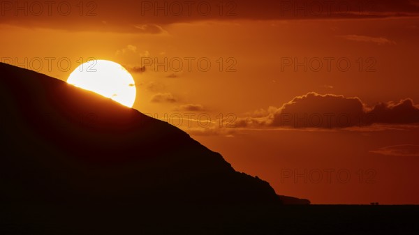 Sun disappears behind mountain, bright warm orange sky at sunset, sunset, Kassos, Karpathos,