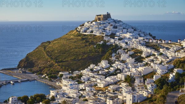 A fortress overlooks a coastal landscape of white houses gently sloping down to a blue sea, Querini