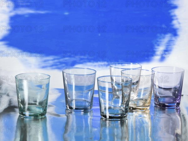 Various glasses on silver foil, blue coloured surface behind, studio shot