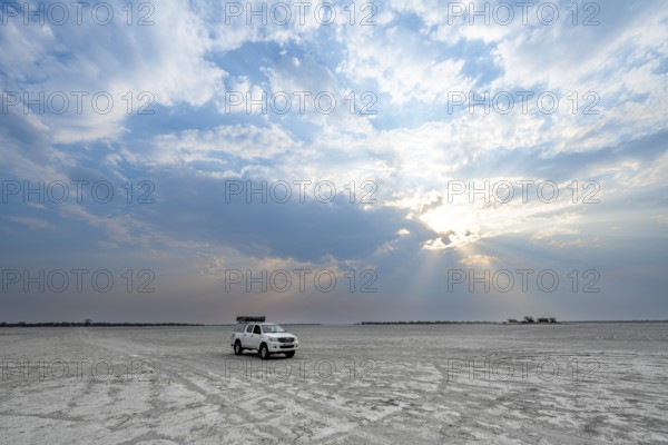 Toyota Hilux off-road vehicle on a salt pan, dramatic clouds with sunbeams, wide open plain, Nxai
