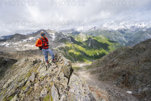Mountaineer on a steep rocky ridge, at the summit of Lasörling, view of mountains of the Venediger