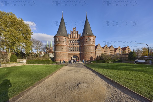 City gate, historic brick building, footpath made of sand, garden with lawn, trees, blue sky with
