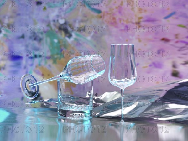 Various glasses on silver foil, behind them various splashes of colour, studio shot