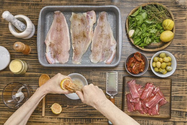 Hands squeeze lemon juice to prepare a marinade for fish fillets arranged in a baking tray