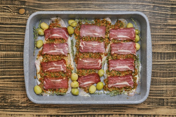A beautifully arranged dish of thinly sliced meat is placed on a baking tray. The meat is topped