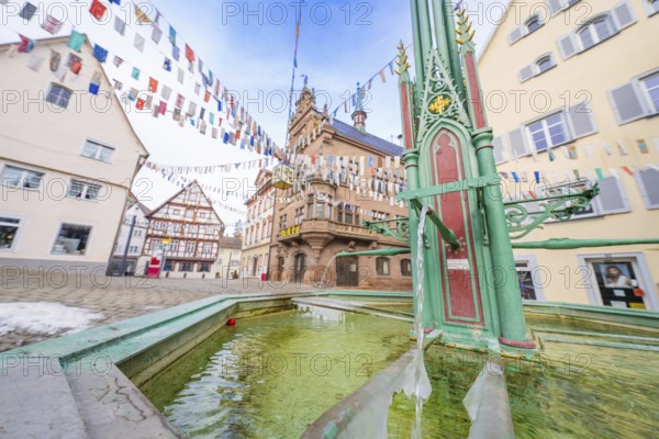 Historic fountain in an old town with colourful pennants and surrounding architecture, Wend