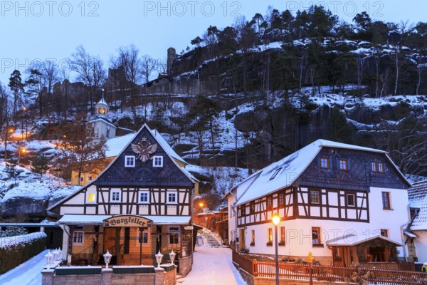 Striking half-timbered houses and mountain church in front of Mount Oybin with ruins, snow and