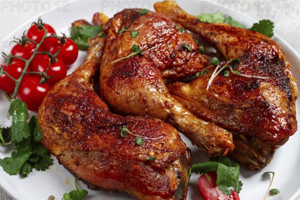 Grilled fried chicken legs, served, with fresh cherry tomatoes, and herbs, on a white plate,