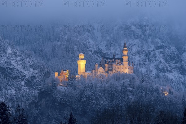 A magnificently illuminated castle at night, surrounded by a snow-covered landscape,