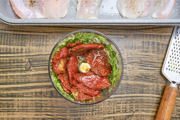 Fresh herbs, garlic and dried tomatoes are combined in a blender bowl. A baking tray with seasoned
