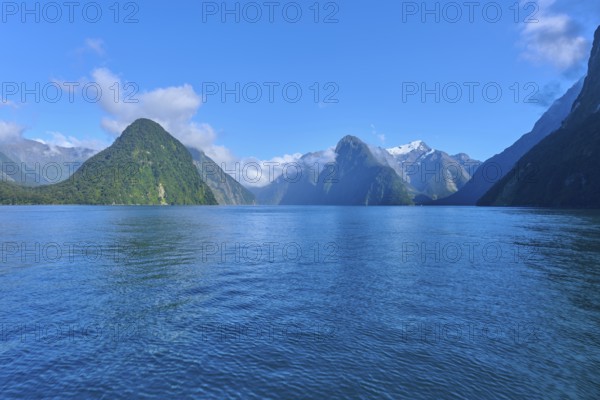 Expansive water surface against a majestic mountain backdrop and blue sky, summer, Milford Sound,