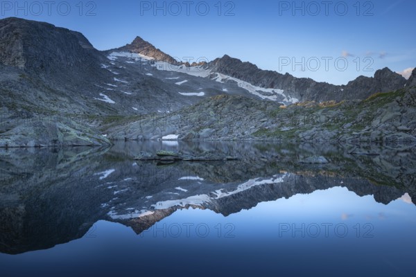 Reflection of snow-covered mountains on a calm water surface under a blue sky at sunrise, Krimml,