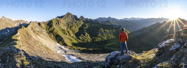 Mountaineer in front of mountain landscape at sunrise, sun star, view of mountain peaks of the