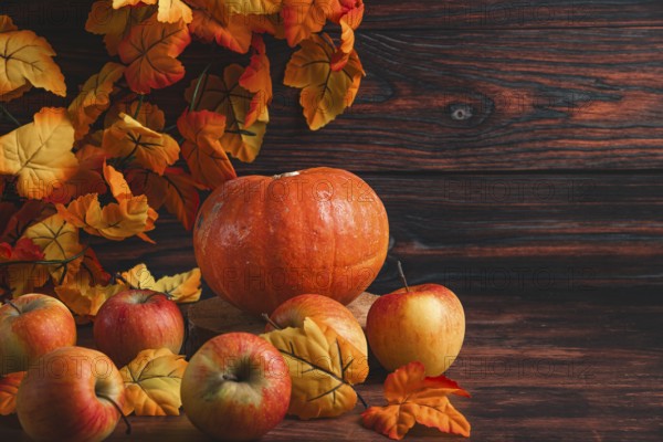 Autumnal arrangement with pumpkin and apples and colourful leaves on wood