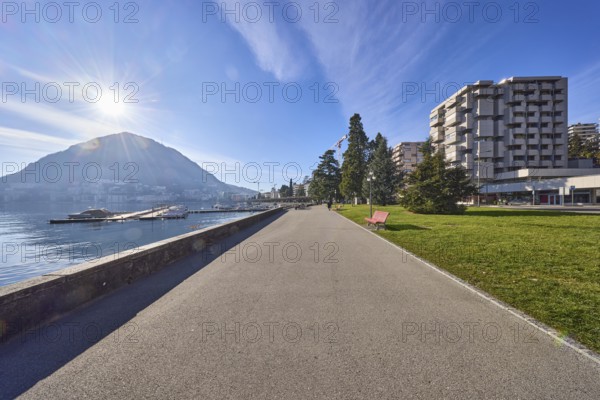 Lakeside promenade, lake, modern architecture, trees, backlight of the sun, blue sky with veil