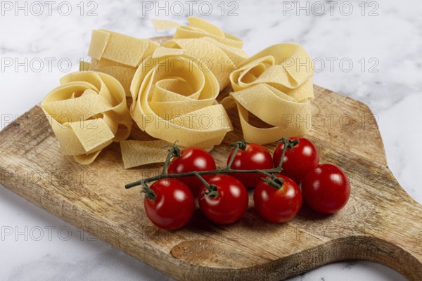 Raw pappardelle pasta, on a wooden chopping board, with cherry tomatoes, top view, no people