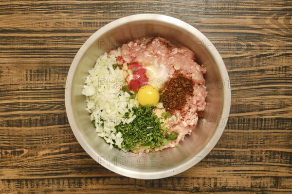 A metal mixing bowl holds a blend of ground meat, chopped onions, herbs, smoked paprika, egg, and