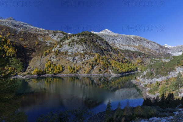 The Galgenbichl reservoir with a mountain forest in fall foliage on a bright sunny morning. Seen