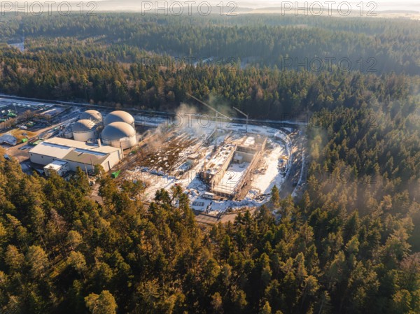 An industrial plant lies in the wintry forest, construction site with cranes, covered with snow,