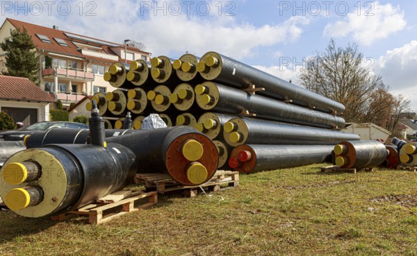 Stacked district heating pipes with yellow ends lie piled up in a meadow