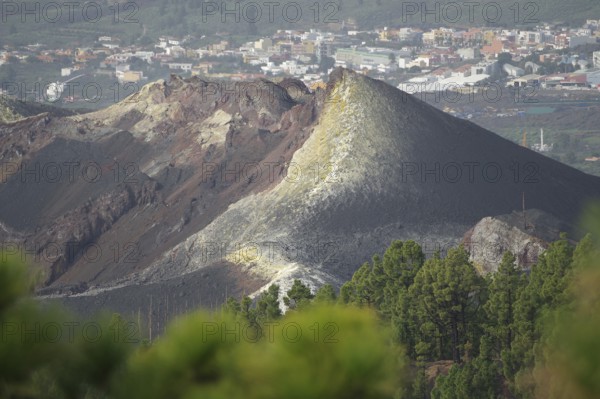 Steep volcano with visible lava and ash layers, city in the background, last volcanic eruption of