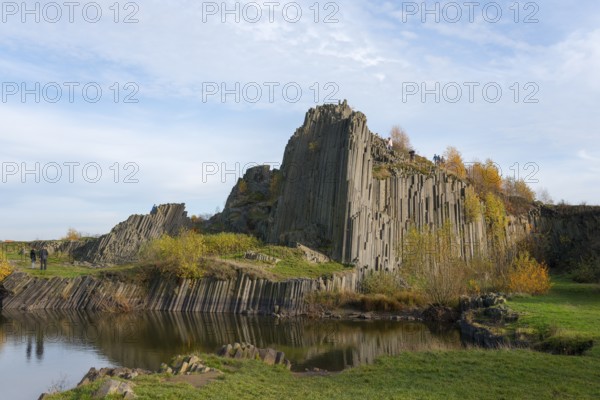 Mighty basalt formations rise under a blue sky, surrounded by autumnal greenery, manor house rocks,