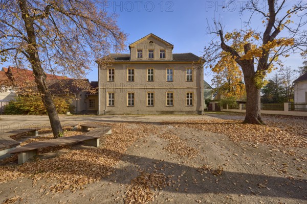 Two-storey building with pointed roof and dormer, autumnal trees, benches, school square, Mühlberg