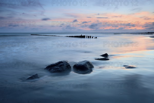 Sunset on the beach, boulders and old groyne in the surf, Klintholm Havn, Møn Island, Denmark,