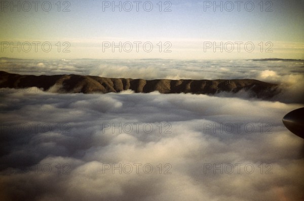Oblique view of a mountain ridge emerging from the cloud cover, location unknown, Australia 1956