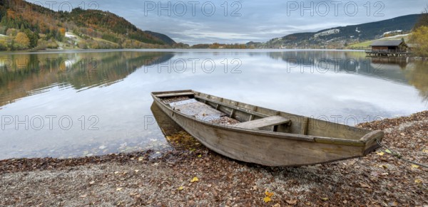 Traditional wooden rowing boat on the shore of Lake Schliersee in autumn, first snow on the slopes,