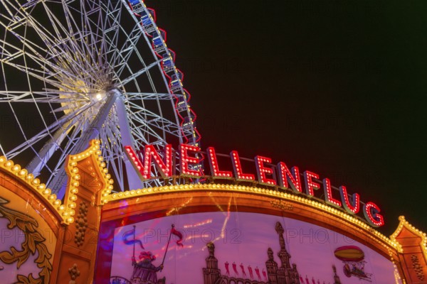 Luminous merry-go-rounds and a Ferris wheel at night at a funfair, Europa Rad, rides, wave flight,