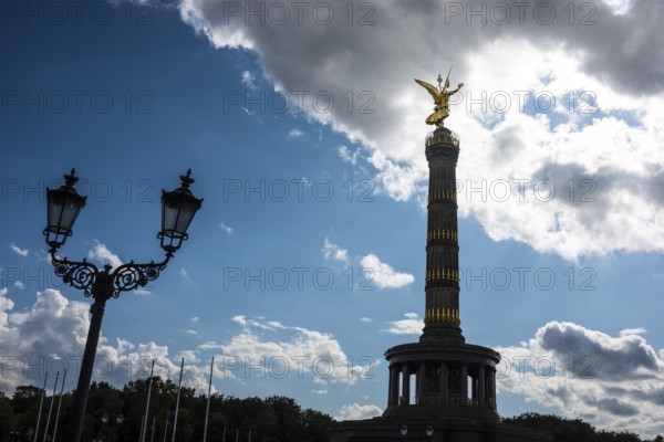 Victory Column next to an old street lamp in a dramatically cloudy sky with balu areas, towering
