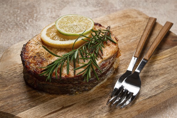 Salmon steak, fried, on a cutting board, top view, rosemary, lemon and lime, homemade, one serving,