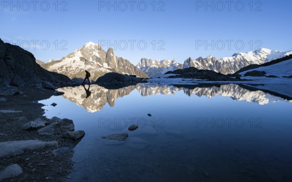 Mountaineer, silhouette in front of mountain landscape in the evening light, water reflection in