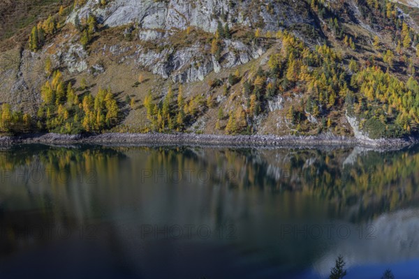 The Galgenbichl reservoir with a mountain forest in fall foliage on a bright sunny morning. Seen