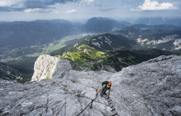 Mountaineer with helmet climbing on the rock in a secured climb, on a narrow rocky ridge, in steep
