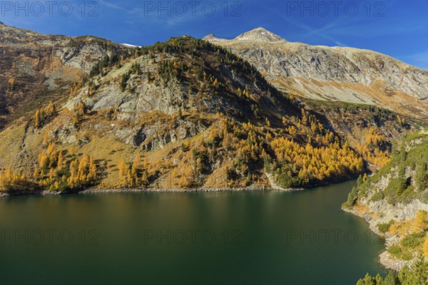 The Galgenbichl reservoir with a mountain forest in fall foliage on a bright sunny morning. Seen