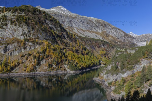 The Galgenbichl reservoir with a mountain forest in fall foliage on a bright sunny morning. Seen
