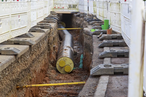 Construction trench with installed district heating pipes and safety fences at a construction site