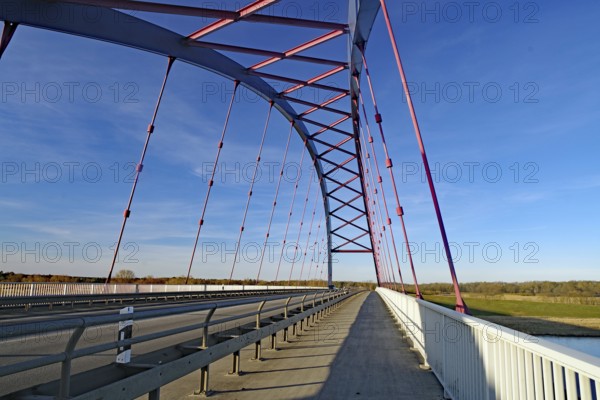 A modern steel bridge with pink and white struts spans a long distance under a clear sky, symbol of